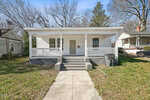 A small, white single-story house at 143 Burwell Avenue, Henderson NC, with a covered porch and three steps leading up to the front door. The house is surrounded by bare trees and similar