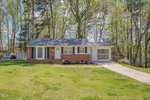 A one-story brick house with white trim, located at 1563 Oakdale Circle in Henderson, NC, features a gabled roof and an attached garage. The home is surrounded by a lush,