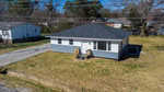 Aerial view of a small, single-story house located at 1841 Garland Street in Henderson, NC, with a gray roof and white siding, featuring front steps. The house is surrounded by a