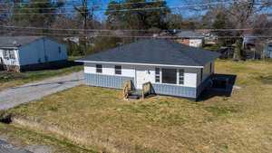 Aerial view of a small, single-story house located at 1841 Garland Street in Henderson, NC, with a gray roof and white siding, featuring front steps. The house is surrounded by a