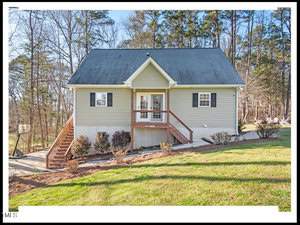 A two-story beige house at 490 Flanagan Road, Henderson NC, with a gabled roof, featuring a wooden front staircase leading to a central door, surrounded by a well-manicured lawn