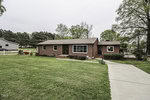 A single-story brick house at 1060 Vicksboro Road, Henderson NC, with white-framed windows, a well-kept lawn, and trees surrounding the property. A concrete walkway leads
