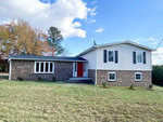A split-level house at 2548 Glebe Road, Henderson NC, with a red door, brick on the bottom level and white siding on the top, under a blue sky with scattered clouds.