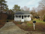 A small, single-story white house with a black roof and an enclosed front porch, situated at 110 Fox Run in Henderson NC, features a yard with bare trees and a driveway to the left,