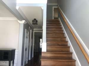 Interior of a home showing a wooden staircase with a handrail leading to the upper floor, adjacent to gray-painted walls and a corridor leading to other rooms.