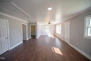 Spacious, empty room with hardwood floors, gray walls, and multiple doors. features ceiling fan, white trim, and natural light streaming in through windows.