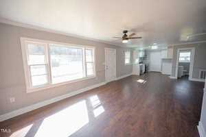 Bright, spacious room with shiny hardwood floors, white walls, large windows, and a ceiling fan. door leads to another room. sunlight casts shadows on the floor.