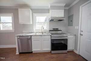 A modern kitchen with white cabinetry, granite countertops, stainless steel appliances, and a window above the sink. door on the right side leads to another room.