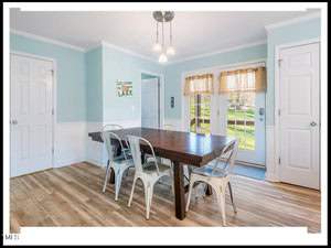 A bright, airy dining room with light blue walls and hardwood floors, featuring a dark wood table, several metal chairs, a hanging light fixture, and doors leading to other rooms.