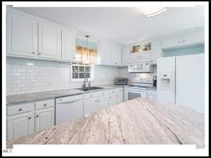 A bright, modern kitchen featuring white cabinetry, stainless steel appliances, subway tile backsplash, and a large island with a textured countertop.