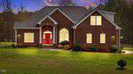 A single-story brick house with a red front door and white trim, lit by exterior lights at dusk, surrounded by a grassy lawn and trees in the background.
