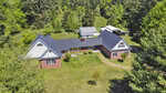Aerial view of a suburban home in Henderson NC with a red brick exterior, black shingle roof, and attached garage, surrounded by lush green trees and a well-kept lawn.