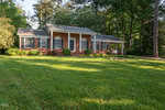 A charming brick house with white columns and windows at 1610 Parker Lane, surrounded by lush green grass and trees bathed in soft sunlight.