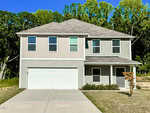 A two-story house at 378 E Waycliff Road, Henderson NC, with a beige and light green exterior, featuring a double garage, a concrete driveway, and a small front porch. There's a small tree and some shrubs in the front yard, with a backdrop of tall green trees and a clear blue sky.