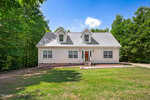 A two-story house with light-colored siding and a gray roof stands at 4011 Shadybrook Drive in Kittrell, set against a green, tree-filled background. The house features two dormer windows and a main entrance with a small porch and steps leading up to it. The front yard is grassy.