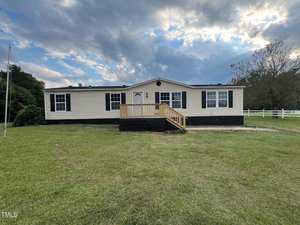 A single-story manufactured home with beige siding and a black foundation sits on a grassy lawn at 805 Morgan Road in Henderson. It features a small wooden porch with steps leading to the front door. The sky above is partly cloudy, and there's a tree and a white fence in the background.