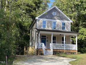 Nestled on 705 Jefferson Street in Henderson, this two-story house boasts beige siding and a dark grey top floor. A charming blue front door opens to a covered porch with white railings, while trees envelop the property, perfectly complementing the driveway in the foreground.