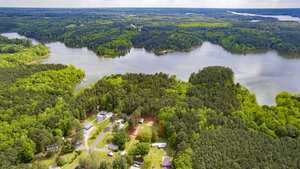 Aerial view of a lush, green forested area surrounding a large lake. Several houses and roads are visible among the trees. A small plot of land is outlined in red, indicating a specific area of interest.