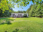 A single-story white house with brown shutters sits at 1207 Barker Road, Oxford. It features a wooden porch and is surrounded by lush trees under a clear blue sky, all set on a large green lawn.