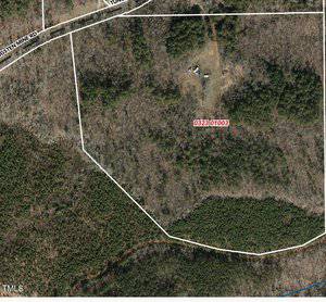 An aerial view of a wooded area with a cleared section. There are visible boundaries outlined, with a property tag labeled "032301003." A road runs along the top left corner, bordered by trees and shrubbery.