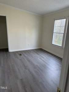 Empty room with light-colored walls and hardwood flooring. A window on the right lets in natural light. An open door on the left leads to a small closet.