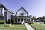 A small, modern two-story house at 115 York Drive features gray siding and a covered front porch, set on a well-maintained green lawn. Surrounded by trees in the charming suburb of Oxford, it basks under a clear blue sky.