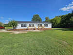 A single-story house with white siding and dark shutters sits on a spacious green lawn at 5714 Days Mill Road in Rougemont. It features two small wooden decks at the front, and a red truck is parked in the driveway to the left under a clear blue sky.