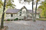 Nestled at 4031 Peace Mountain Road, this beige A-frame house in Oxford features a large triangular window and cozy porch. Surrounded by woods with vibrant fall foliage, the ground is adorned with gravel and scattered leaves.