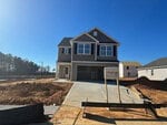 The newly constructed two-story house at 101 Long Green Way boasts a sleek gray exterior and a double garage. Nestled in Oxford, the surrounding area buzzes with construction, displaying exposed soil and building materials beneath a clear blue sky.