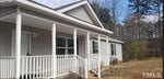 Nestled in Franklinton, the single-story gray house at 4073 Pine Ridge Road features a charming white porch railing and columns. With multiple windows and a welcoming front door, it sits amidst a grassy yard and trees under a partly cloudy sky.