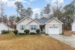 Located at 1198 E Middleton Drive in Creedmoor, this beige single-story house features a gabled roof and an attached garage. A neatly trimmed lawn complements the paved driveway, while a few bushes add charm to the front. Tall trees stand in the background under a partly cloudy sky.