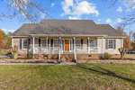 Nestled at 118 W Quailridge Road in Oxford, this charming one-story house boasts a gray roof and beige siding. Featuring a front porch with white railings and a wooden door, it is surrounded by a grassy lawn and leafless trees under a partly cloudy sky.