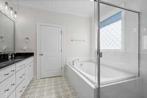 A modern bathroom featuring a large glass-enclosed bathtub with a tiled surround, white cabinets with black countertops, a wall mirror, and patterned floor tiles. Natural light enters through a window with a decorative privacy film.