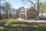 Nestled in Youngsville, the two-story house at 60 Hidden Cove Court boasts stone and siding with large windows and a steep gabled roof. A curved walkway leads to the entrance, surrounded by a well-maintained lawn and trees, with a wooded area and clear blue sky as its backdrop.