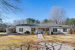 Located at 891 Green Hill Road, this single-story Franklinton house boasts white siding and a dark gray roof. The inviting front porch with columns complements the spacious yard, where sparse grass and surrounding trees create a serene setting on a clear, sunny day.