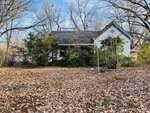 A small, white, weathered house on 210 King Street is surrounded by bare trees and bushes. The ground is covered in dry, fallen leaves, creating a rustic Oxford autumn atmosphere. The house features a gabled roof and appears secluded in its wooded area.