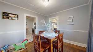 A dining room with a wooden table and four chairs. A small centerpiece is on the table. A colorful rocking horse is on the floor, and a large decorative letter "E" hangs on the wall. A chandelier hangs from the ceiling.