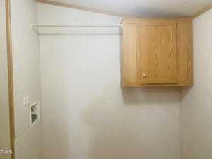 A small room with light-colored walls featuring an empty closet rod and a wooden cabinet on the wall. The area is otherwise bare, providing a minimalistic appearance.