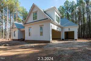 Newly constructed two-story house with white siding and a two-car garage, surrounded by trees. The blue sky is visible above. A date, "2.3.2024," is written at the bottom of the image.