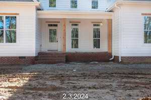 A white house with a brick front porch under construction, featuring large windows and a door. The ground is unpaved with visible dirt and construction debris. The date "2.3.2024" is overlaid at the bottom.