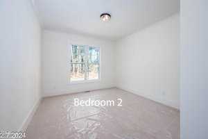 A bright, empty bedroom with white walls, a large window showing a wooded view, carpeted floor covered with protective plastic, and a ceiling light fixture. The words "Bedroom 2" appear over the floor.