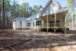 A newly built white house with a covered porch sits among tall pine trees. The date "2.3.2024" is overlaid at the bottom of the image. The ground is bare, indicating recent construction.