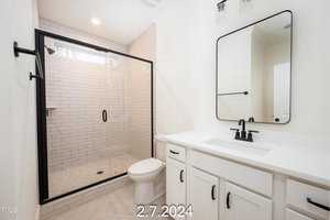 A modern bathroom with a glass-enclosed shower featuring white subway tiles. There's a white countertop with a black faucet and a rectangular mirror above it. A toilet sits next to the vanity. Soft lighting illuminates the space. Date: 2.7.2024.