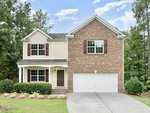 This charming two-story house at 1825 Fillmore Drive in Creedmoor features a brick and siding exterior, double garage, and inviting covered front porch. The well-maintained lawn, adorned with shrubs and small trees, complements the partly cloudy sky as the driveway leads to the spacious garage.