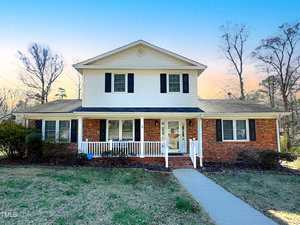 The two-story suburban house at 114 Forest Road, Oxford, features white siding and a red brick facade. It boasts a small front porch with white railings, black shutters, and a manicured lawn. The sky presents a clear gradient from blue to orange, signaling sunset.