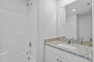 A modern bathroom featuring a white bathtub with a showerhead and a granite-topped vanity. The vanity has a white sink with a chrome faucet and a large mirror above it. The walls are painted white, creating a clean and bright atmosphere.