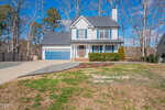 A charming two-story white house on 1649 Rogers Pointe Lane features a blue garage door and a chimney. Nestled in Creedmoor, it sits on a grassy lot with a driveway. A sign declares, "This home is for sale, not for rent." Surrounded by trees and offering a fenced backyard, it's an inviting residence.