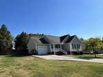 Located at 110 Carriage Hill Drive, this charming single-story house boasts light-colored siding and a dark roof. With a welcoming front porch, attached garage, and a driveway that stems from the street, it's nestled amid grassy lawns and trees under the clear blue sky.