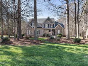 Nestled at 1173 Smith Creek Way in Wake Forest, this two-story house boasts a gray exterior, surrounded by tall trees and a well-maintained lawn. With its large front porch and multiple gables, the home exudes warmth and spaciousness amidst its serene, wooded setting.