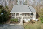 A quaint two-story house at 505 Crescent Heights Drive, featuring a gray roof and beige siding, sits in a wooded area of Creedmoor. It boasts a screened front porch with steps leading to the door. A gravel driveway lies in the foreground, with a satellite dish on the right.